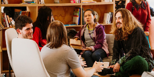 A group of students sat in the SU living room chatting and smiling